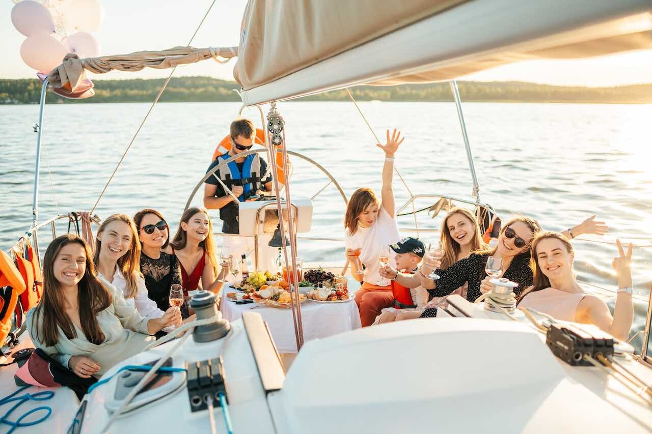 Group of girl friends sitting on back of catamaran yacht enjoying the sunset and smiling for camera at Ibiza catamaran cruise
