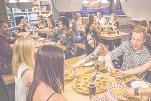 Friends sitting at table reaching for pizza slices