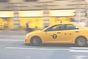 Yellow taxi moving along road in city