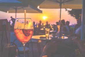 Close up of cocktail at bar with setting sun overlooking beach in background