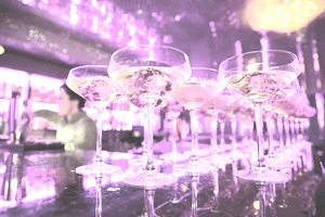 Cocktail glasses lined up on bar with bright lights behind
