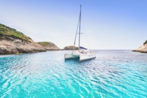 Catamaran sailing on crystal blue island waters with blue sky in background