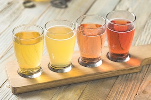 Four glasses of different coloured ciders on wooden serving tray on table