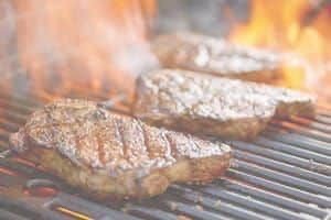 Close up of steak sizzling on grill with flames