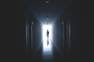 Person walking down dark mysterious corridor towards light