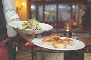 Server holding two plates on one arm with Spanish cuisine