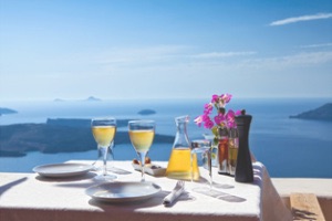 Wine, flowers and fine dining set table over looking dark blue waters of Santorini island