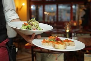 Man extending arms with 2 courses for guests in French restaurant