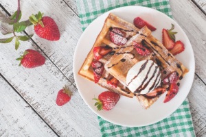 Birds eye view of waffles with strawberries, drizzled chocolate and ice cream, colourfully decorated with strawberries
