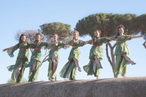 Greek dancers lined up on outdoor stage, holding shoulders and smiling
