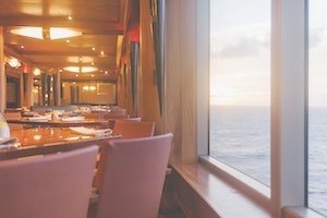 Pink chairs and dining table adjacent to boat window with ocean in background