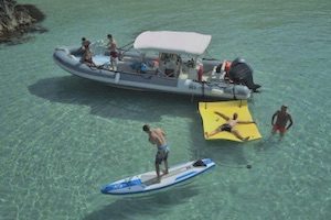 Aerial shot of speed boat with guests on board + man standing on stand up paddle board