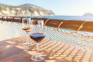 Two wine glasses sat on wooden table overlooking beach and cliffs in background