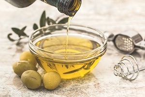 Clear bowl of olive oil with fresh olive oil branches in background