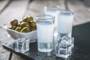 Shots of ouzo with ice cubes and bowl of olives on plate