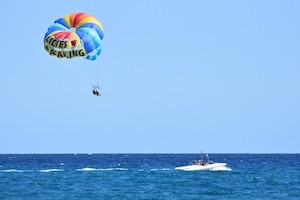Ski boat on open seas with parasailers out back sitting underneath colourful parachute