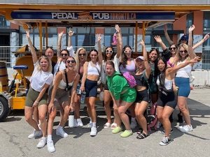 Group of girls smiling and posing in front of Toronto Pedal Pub bike