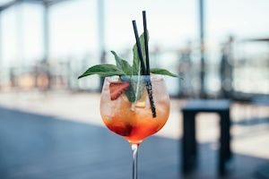 Aperol Spritz served in tall cocktail glass with background view of rooftop overlooking city