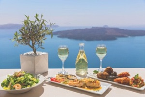 Seafood meal with wine sitting on white table overlooking blue waters of Santorini island