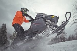 Man in orange jacket in snowmobile ploughing through thick powder
