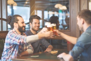 Guys smiling and cheersing with beer around table
