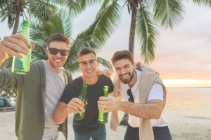Friends smiling and laughing with beers in hand on tropical beach