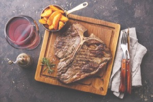 Birds eye view of t-bone steak with fries and rosemary on wooden square block