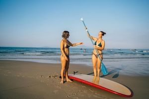 Girls standing on beach with stand up paddle board