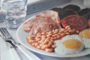 Traditional English breakfast including bacon, baked beans, tomato and fried eggs served on plate with knife and fork to the left