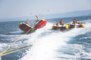 4 friends on boat tube with 2 about to fall into ocean spray