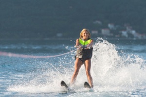 Woman standing and smiling on two water skis and water spraying behind her