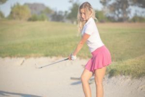 Girl in sexy pink golf skirt about to hit ball from sand bunker