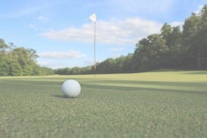 Golf ball sitting on green near hole & flag