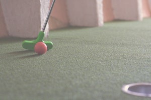 Golf putter about to push golf ball into hole on mini golf course